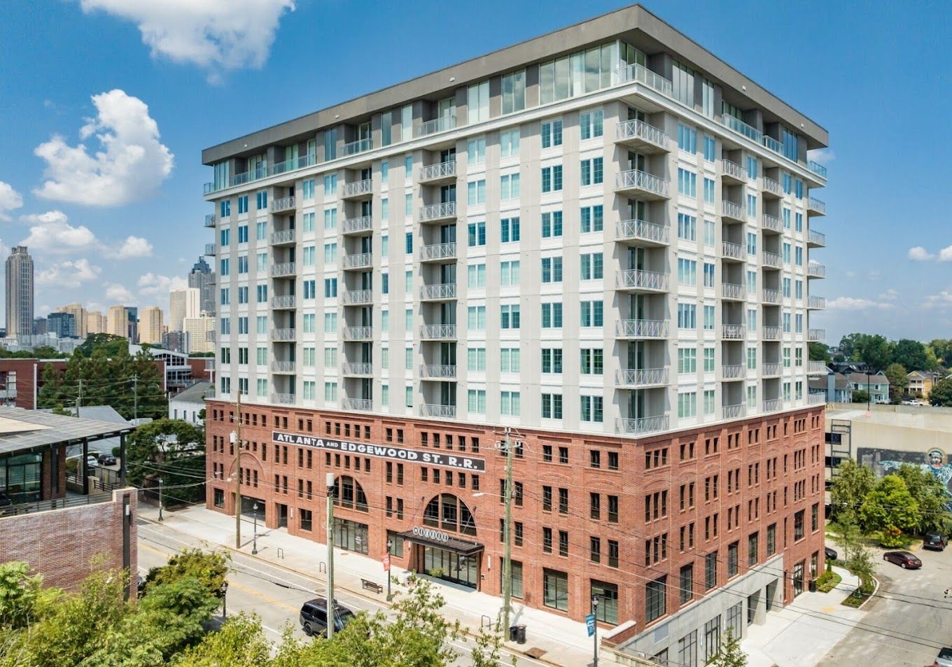 Modern multi-story building with brick and glass facade, featuring balconies and situated on a city street.